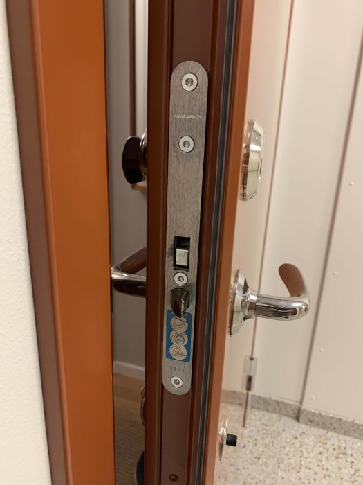 Dörrlås från ASSA ABLOY installerat på en öppen brun dörr, med fråga om passande Yale slutbleck.