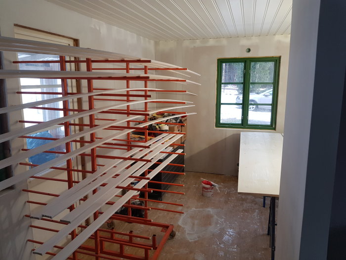 Nymålade vita lister ligger på röda bockar i ett rum under renovering med synligt fönster.