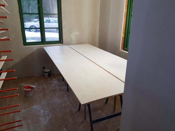Renoveringsrum med grundmålade lister och obrutna träskivor på arbetsbord framför ett fönster.