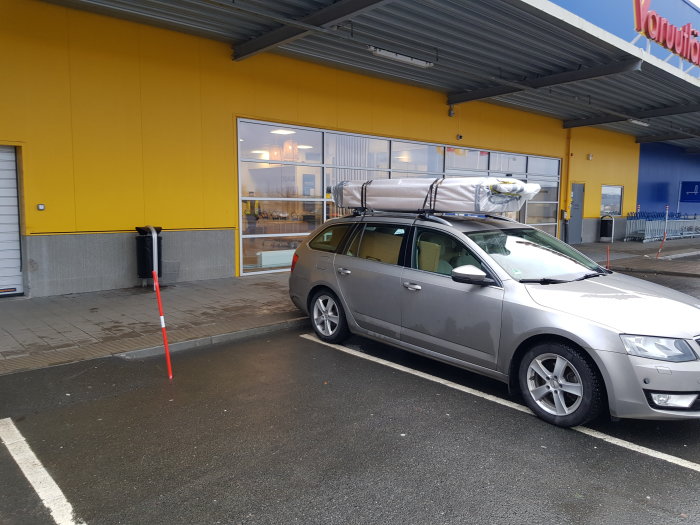 Bil parkerad utanför byggvaruhus med flera stora skåppaket lastade på taket.