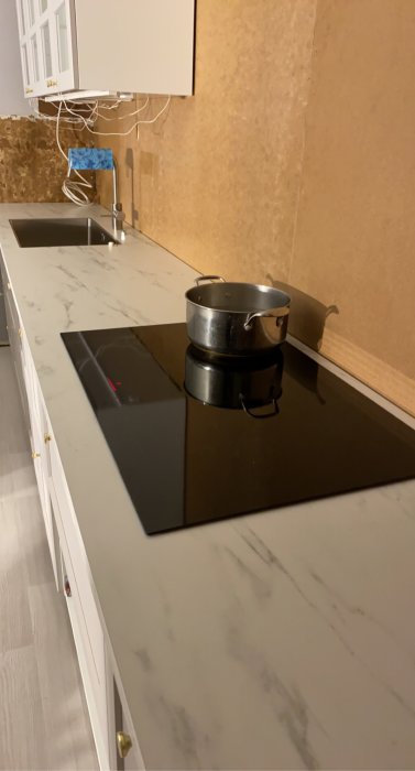 Nyinstallerad spishäll med en kastrull ovanpå i en köksmiljö med oskyddade väggar och elinstallationer.