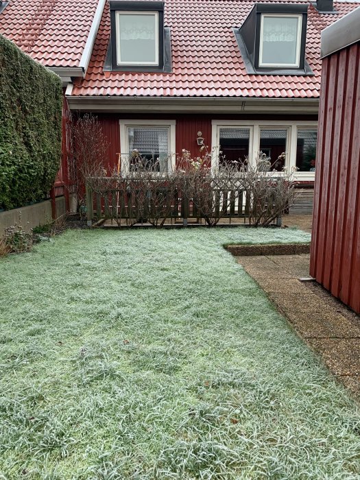 Radhus med röd fasad och tegeltak, frostig gräsmatta framför, vinterdag.