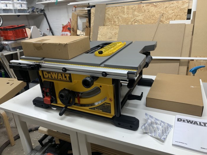 Nyuppackad bordscirkelsåg av märket DeWalt på ett arbetsbord i en verkstad, omgiven av kartonger och förpackningsmaterial.