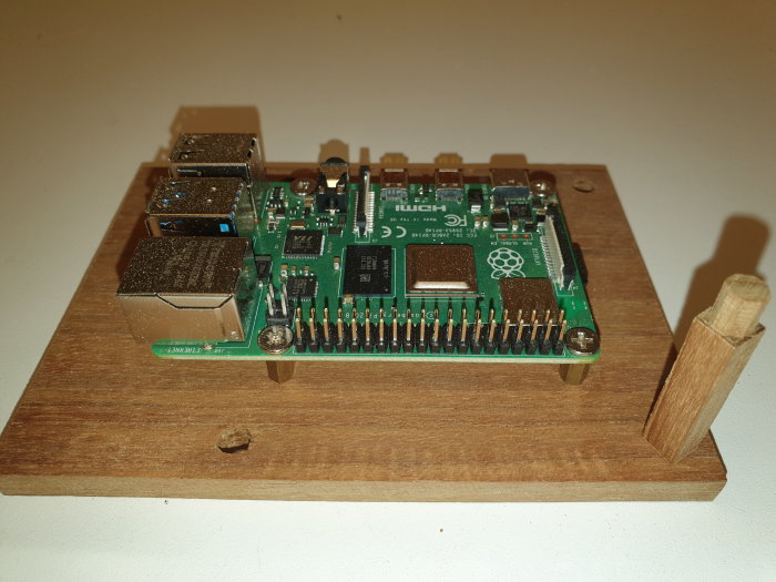 Sexkantig wooden dowel fäst vid en träplatta bredvid ett monterat Raspberry Pi-kort, arbete i process.