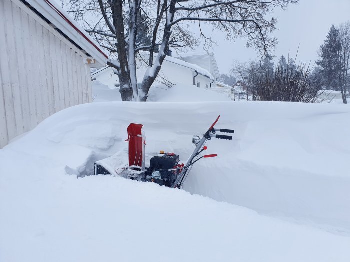 Nyinköpt röd snöslunga bland höga snödrivor nära en byggnad under en snötäckt dag.