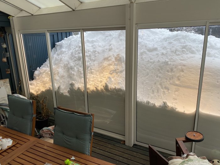 Snödrivor upp mot glasade uterumspaneler från insidan av ett hem i Västerbotten, synlig tyngd och volym av snön.