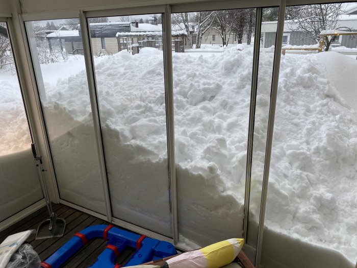 Utsikt från ett glasat uterum med stora snödrivor pressade mot fönstren i en villa i Västerbotten.