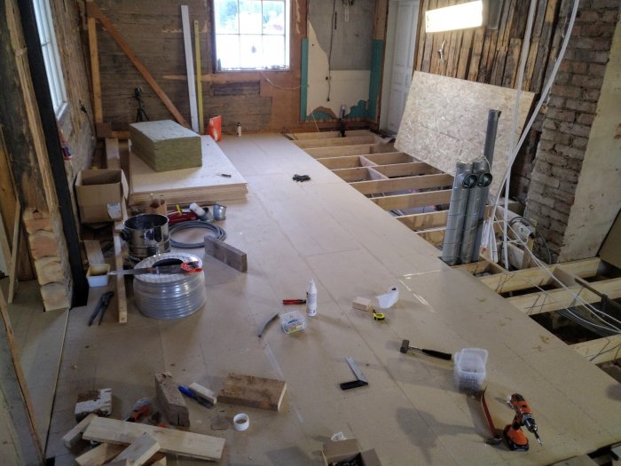 Renoveringsprojekt av ett rum med nytt oslaget golv, byggmaterial och verktyg utspridda.