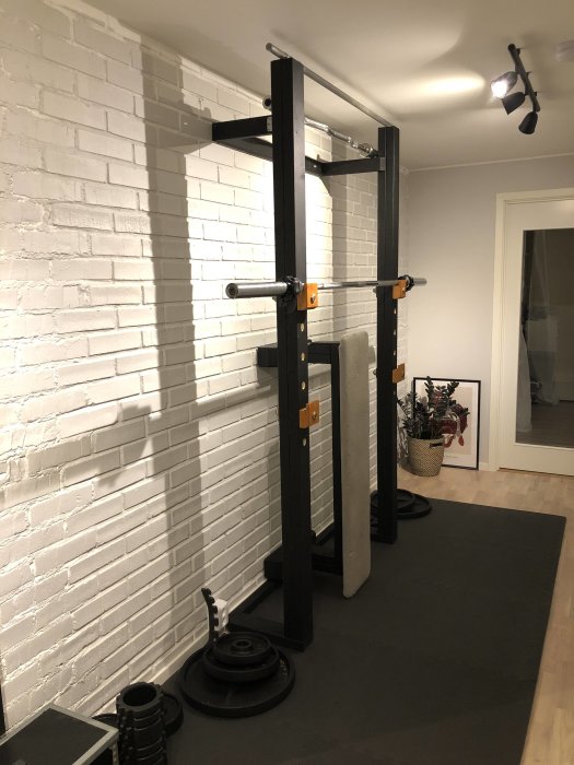 Hemmagym med squat rack och viktskivor i en korridor med vit tegelvägg.