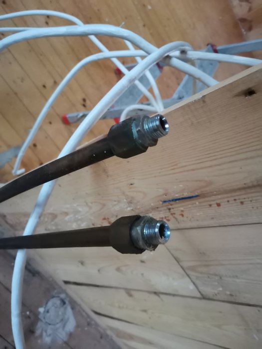 Två exponerade vattenrör med öppna ändar framför en trävägg, tillfällig lösning efterfrågas.