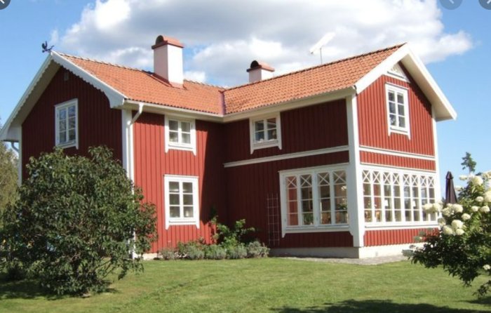 Rödmålat nationalromantiskt 1.5-plans trähus med vita knutar och många fönster, byggt i vinkel.