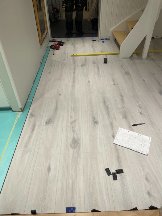 Nyinstallerat laminatgolv i hall med trappa, verktyg och distansklossar synliga, kvartslist ej i bild.