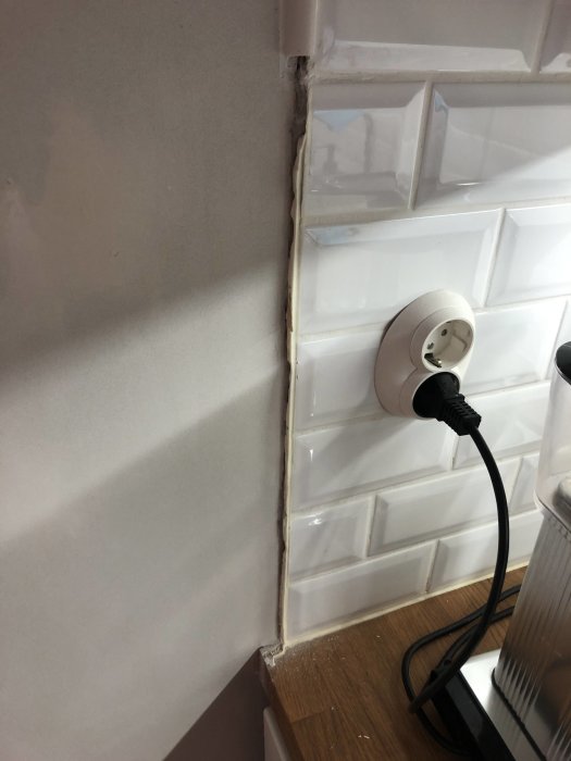 Köksvägg med vit kakel där pärlspont avlägsnats vilket blottat en oväntad kant och eluttag på väggen.