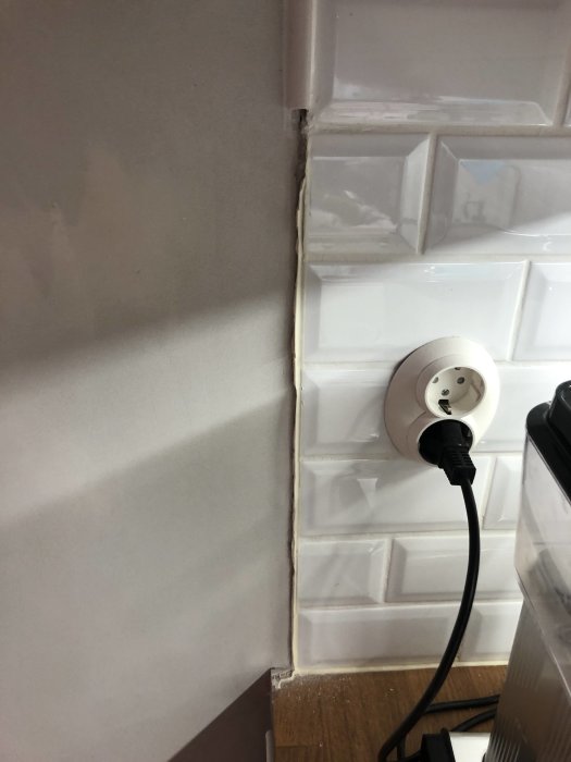 Ojämnheter vid avslutningen av vitt kakel i kök efter borttagning av pärlspont, med synligt vägguttag.