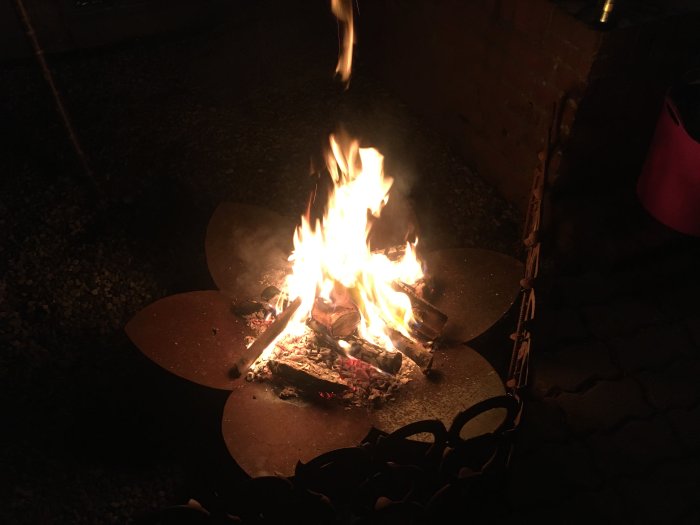 Eld brinner i ett hemmagjort eldfat utomhus i mörkret som stämningsbelysning vid korvgrillning.