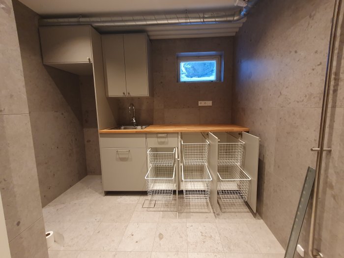 Kök med elfa trådbackar på glidskenor under arbetsbänk och grå skåp ovanför.