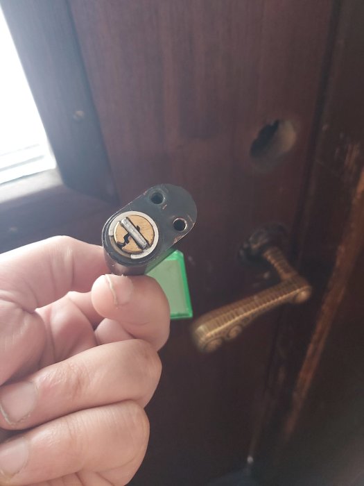 Hand håller urtaget låscylinder framför en stängd dörr med ett synligt låshål.