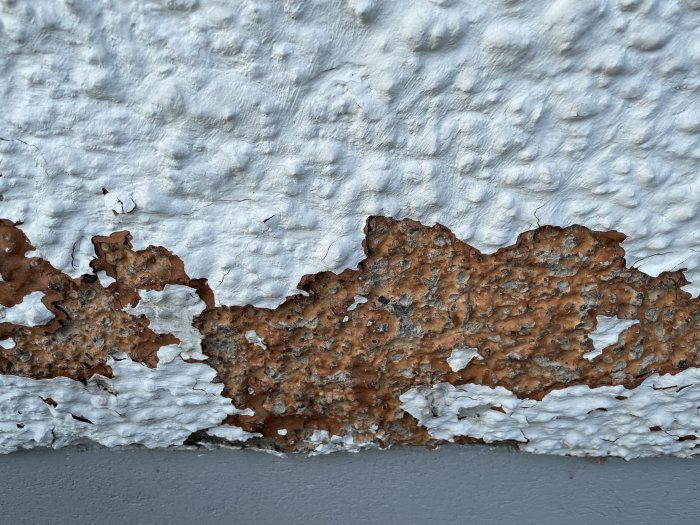 Skadad fasad med vit färg som flagnar och avslöjar underliggande laxrosa kalkputs.