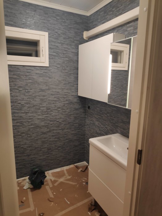 Renoverat badrum med nytt kakel och monterat vitt skåp ovan handfat, byggavfall på golvet.