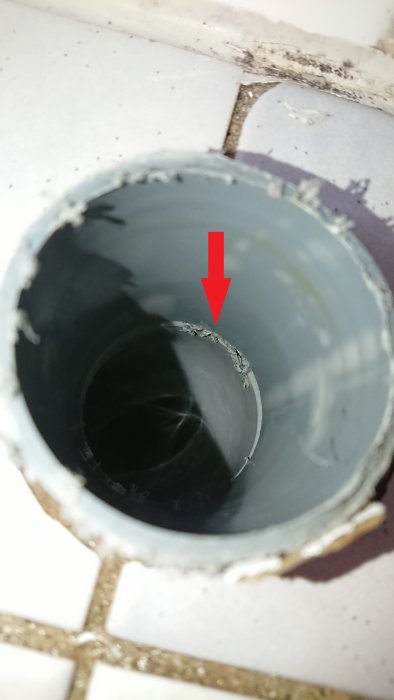Närbild på ett avhugget plastavloppsrör med ett synligt hack markerat med röd pil.