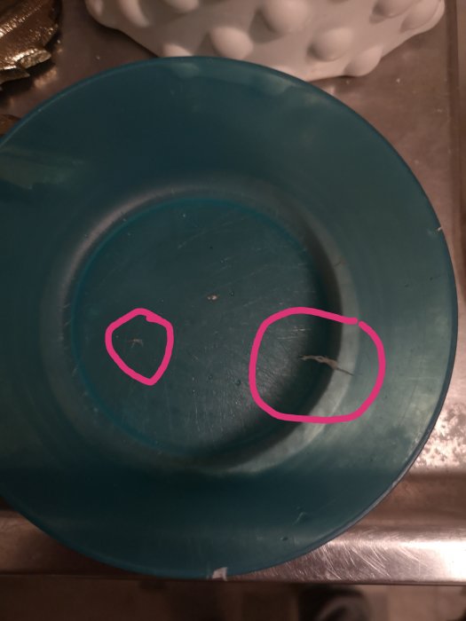 Blå hink med vita klumpar av ättikablandning markerade med rosa cirklar, indikerar svårigheter att lösa upp oidentifierad påväxt.