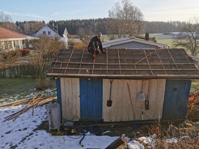 Person byter tak på ett uthus, gammalt tegel borttaget, ny takpapp och ströläkt på plats.