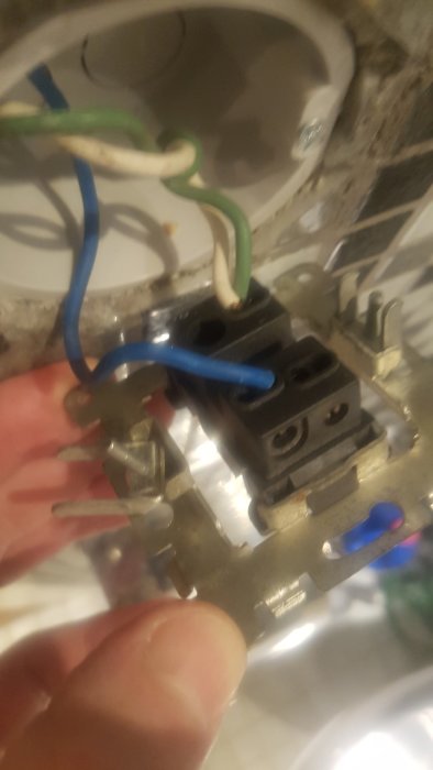 Hand håller en demonterad elektrisk uttagsfront med synliga kablar och anslutningar.