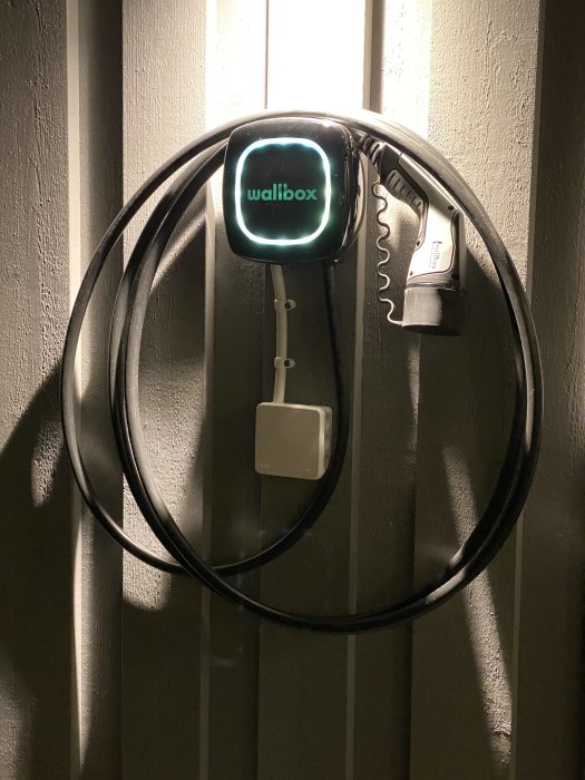 Väggmonterad elbilsladdare "Wallbox" med upphängd kabel och laddpistol.