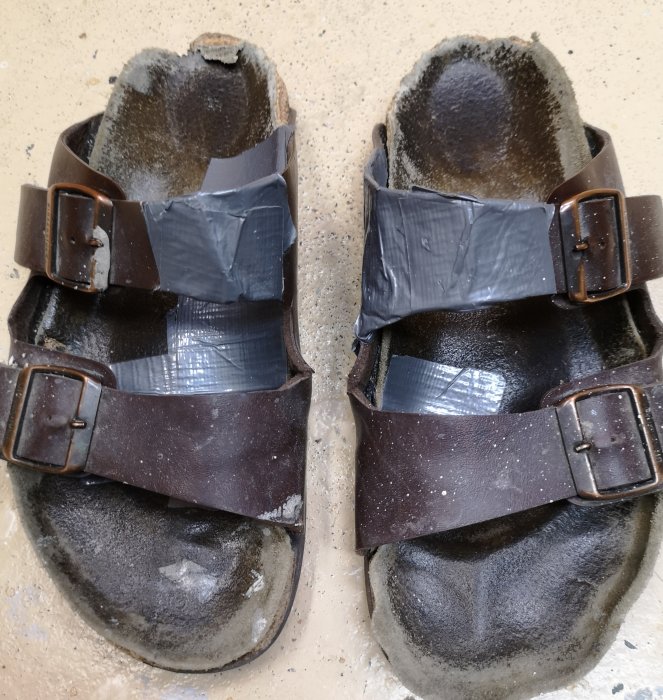 Ett par välanvända Birkenstock-sandaler lagade med silvertejp på remmarna och sulorna.