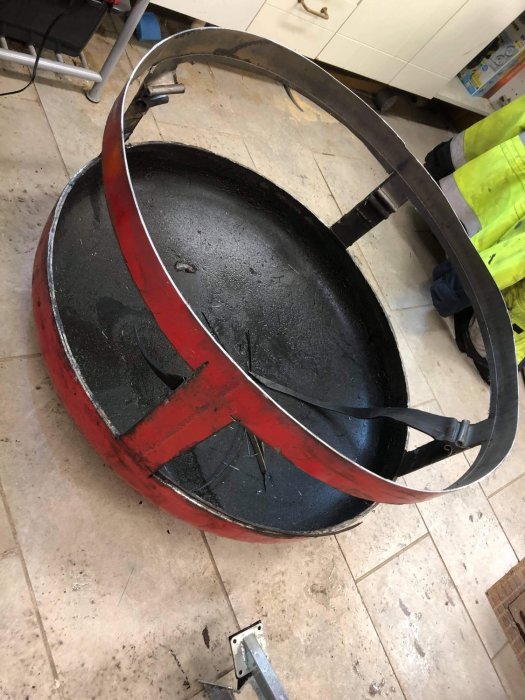 En gammal acktank med rödlackerad kant redo att byggas om till ett eldkärl, står på ett kakelgolv.