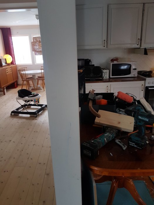 Kök i renovering med verktyg på bord och golv, vita köksskåp och matplats i bakgrunden.