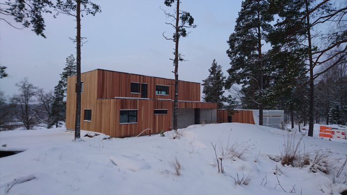 Modern träklädd byggnad i snöigt landskap, kräver underhåll som slipning och oljning.