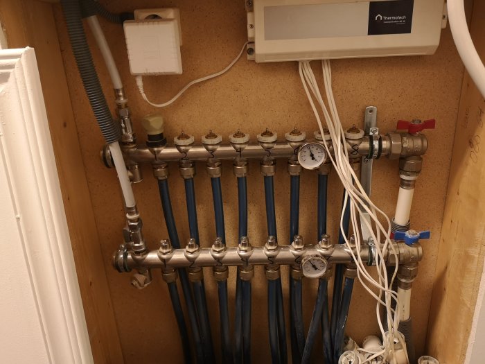 Installationsskåp med vattenledningar, manometer, golvvärme-fördelare och elektriska kablar.