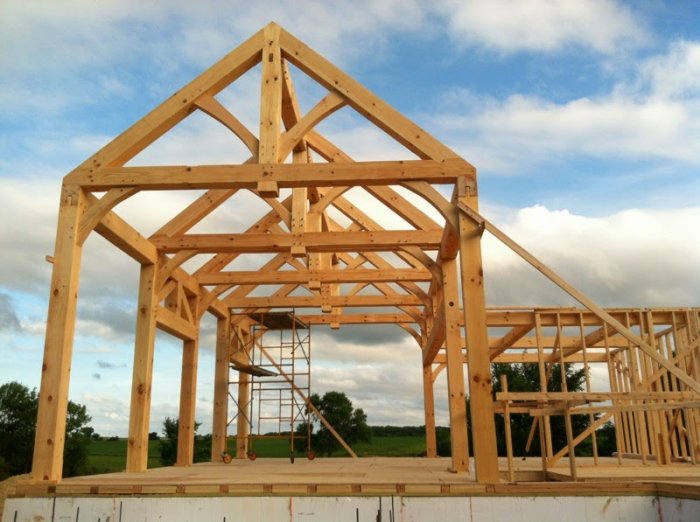 Timber-frame konstruktion under uppbyggnad för ett hus med synliga träbalkar och ställning.