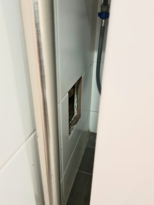 Stort öppet hål i badrumsvägg bredvid en tvättmaskin, tänkt som inspektionslucka.