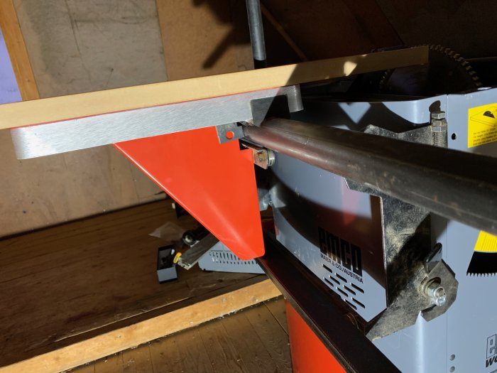 En närbild av ett justerbart aluminiumbord för sågning, med en träskiva placerad ovanpå för att testa passformen.