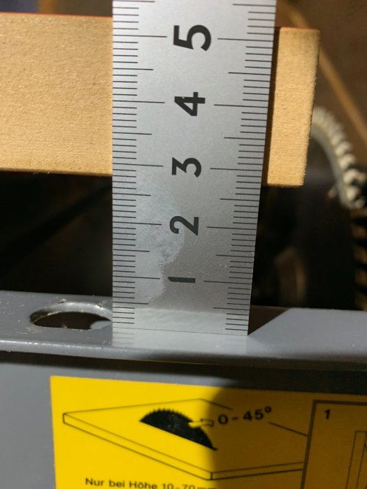 Tumstock mäter tjocklek på justerbord vid verktygsmaskin med skala synlig.
