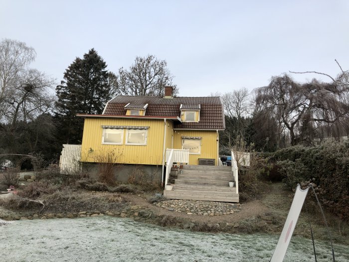 Gult hus byggt 1922 med renoverad fasad och nytt tak, frostig gräsmatta i förgrunden, utan synliga brädhögar.