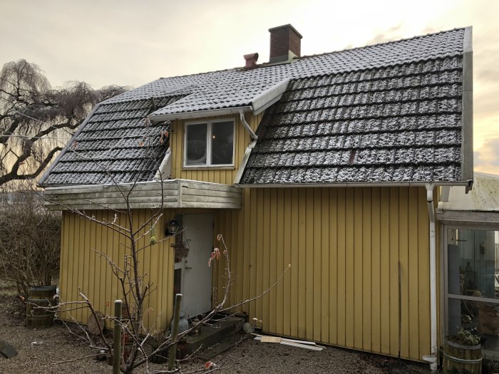 Ett gult hus med en lätt snötäckt tak som nyligen renoverats, synliga bräder och en nybyggd entré.