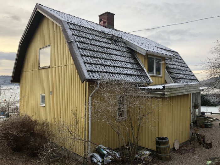 Renoverat gulmålat hus med plåttak och snö, en del renoveringsmaterial syns.