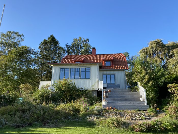 Renoverat hus från 1922 med 4 lager linoljefärg på fasaden och nytt rött tak, omgiven av trädgård.