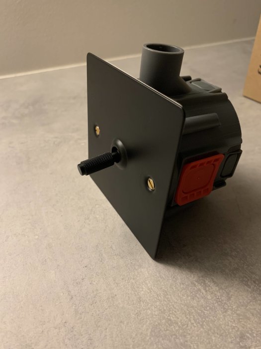 Svart trappbrytare med röd dosa och justerbar svart spak på en ljus yta, redo för installation.