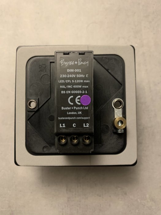 Bakifrånvy av en Buster + Punch DIM-001 ljusdimmer monterad i en väggdosa, med teknisk specifikation synlig.