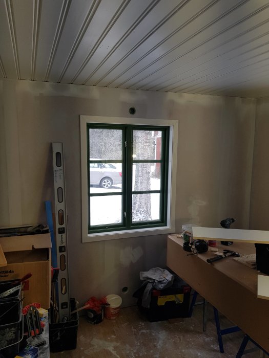 Nyinstallerat grönt fönster med omgivande vita smygar och foder i ett rum under renovering, verktyg och material syns.