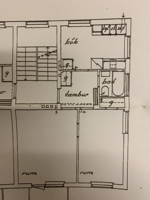 Handritad skiss av en lägenhetsplan med kök, bad och tambur markerade.