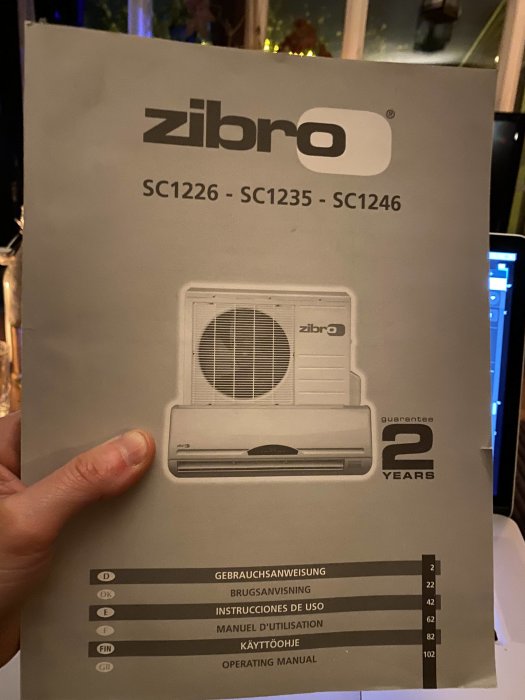 Hand håller en användarmanual för Zibro luftvärmepumpar med modellnummer och flerspråkiga instruktioner.