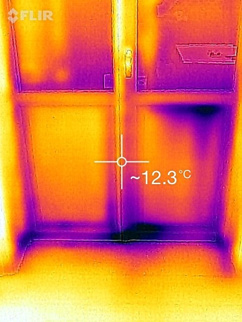 Termisk bild på en dörr med färgspektra som visar värmeutstrålning, tagen med FLIR värmekamera-tillsats för telefon. Temperatur är markerad till cirka 12.3°C.