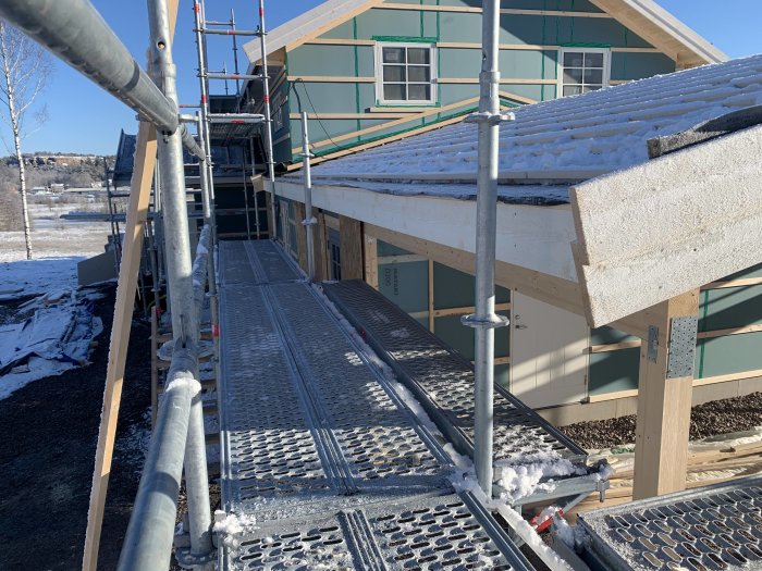 Nyinstallerade pannbrädor på garage och pågående arbete med fotplåtar på hus med snöbelagt tak.