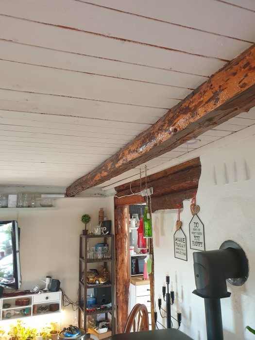 Inredning av ett vardagsrum i en drängstuga med synliga timmerbalkar i taket och en blandad stötta i hörnet.
