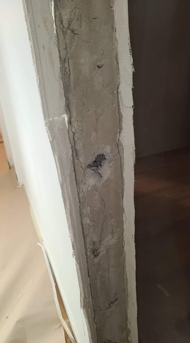 Delvis nedriven gammal dörrkarm med exponerad puts och glasfiberväv i en vägg under renovering.
